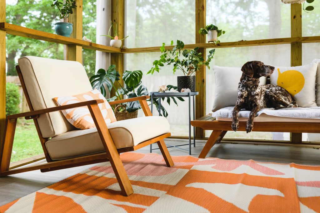 Cozy and stylish sunroom constructed by Bastos Construction, featuring modern furniture, a colorful area rug, and a view of the lush outdoors, perfect for relaxation and enjoying nature.